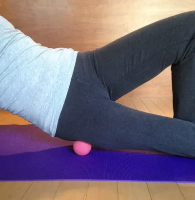 Demonstrates how to use a small ball for muscle relief or massage, likely targeting the hip or glute area.