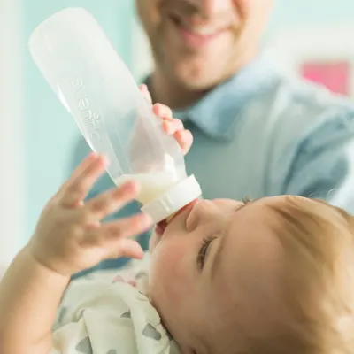 Shows the product being used in a real-life scenario, demonstrating how easy and natural it is to feed a baby with this bottle.