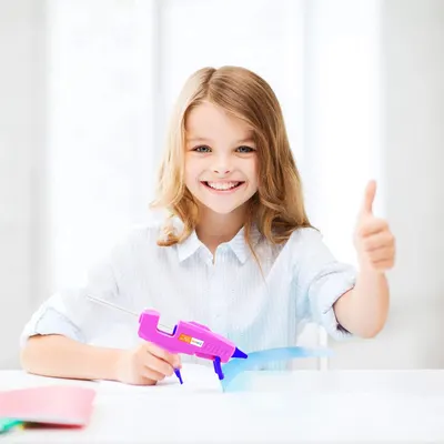 Shows a young girl happily using the product, likely a glue gun, to demonstrate its ease of use and suitability for children's crafts.