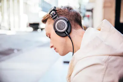 Shows the headphones being worn by a person in a natural outdoor environment to help shoppers visualize how the product looks and fits in everyday use.