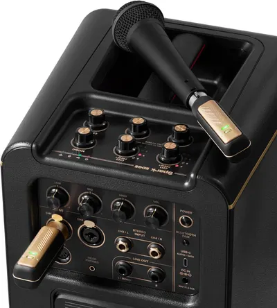 This image showcases the detailed anatomy of the karaoke speaker system, highlighting the control panel with multiple knobs and dials, the microphone storage compartment, wireless microphones, and…