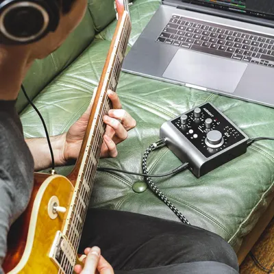Shows the product being used in a real-world home music recording environment to help shoppers visualize how the audio interface fits into their creative workflow.