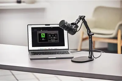 Shows the microphone in a real-world podcasting or streaming setup with a laptop to help shoppers visualize how the product fits into their workspace.