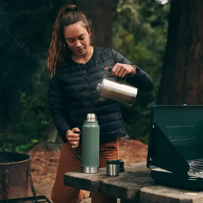 Demonstrates the product in a real-world outdoor camping context to help shoppers visualize using the thermos in nature settings.