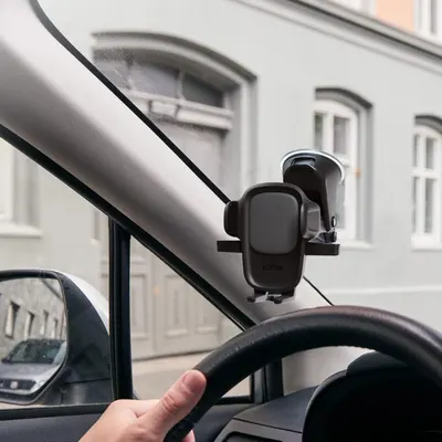 Demonstrates the product in a real-world driving context, showing how it mounts to the windshield for hands-free phone use while driving.