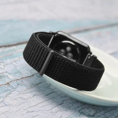 Displays the smartwatch with its black woven band in a clean, lifestyle setting to showcase the product's design and style without distractions.