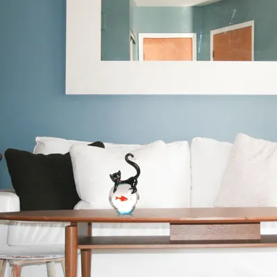 Showcases the product (decorative cat and fishbowl figurine) in a real-world living room environment to help shoppers visualize how it would look in their own home.