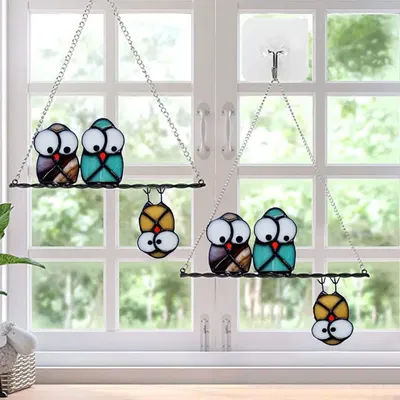 Shows the stained glass owl ornaments displayed in a real home window setting to help shoppers visualize how the product looks when hung and used as decorative window art.
