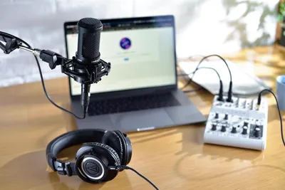 Demonstrates the product in a real-world professional audio recording or streaming context, showing how it integrates into a complete setup with laptop, headphones, and audio interface.