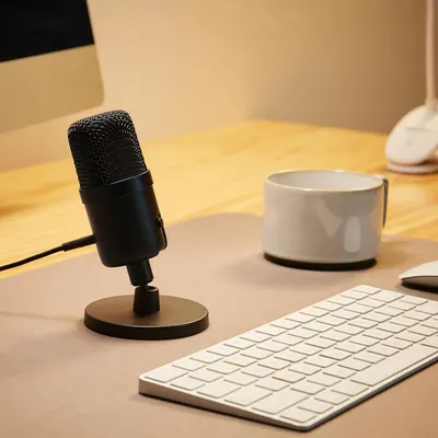 Demonstrates the product in a real-world home office or workspace environment to help shoppers visualize how the microphone fits naturally into their daily work or content creation setup.