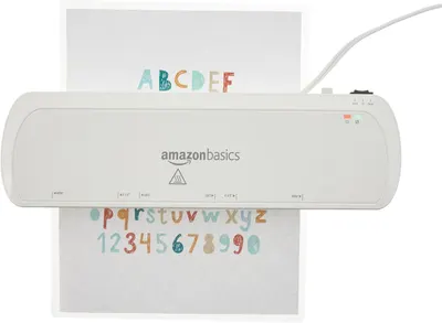 Shows the AmazonBasics laminator in use with a colorful alphabet and numbers sheet being laminated, demonstrating the product in action on a clean white background.