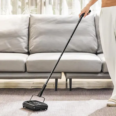 Demonstrates the product being used in a real-world home setting to help shoppers visualize how the manual carpet sweeper works on rugs and floors in their own living space.