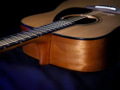 Showcases the acoustic guitar in an artistic, professional setting to emphasize its craftsmanship, premium wood finish, and aesthetic appeal to potential buyers.