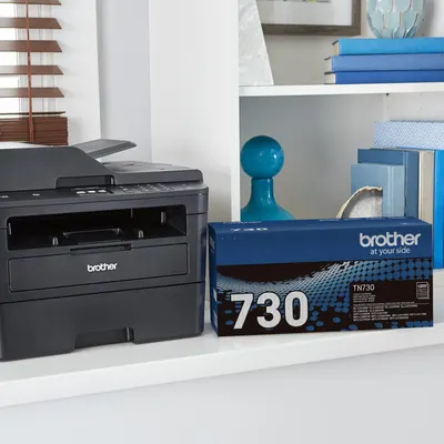 Shows the Brother printer and toner cartridge in a real-world home office environment to help shoppers visualize the product in their own space.