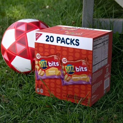 Shows the product in a real-world outdoor setting with a soccer ball to position it as a convenient snack for active lifestyles and sports activities.