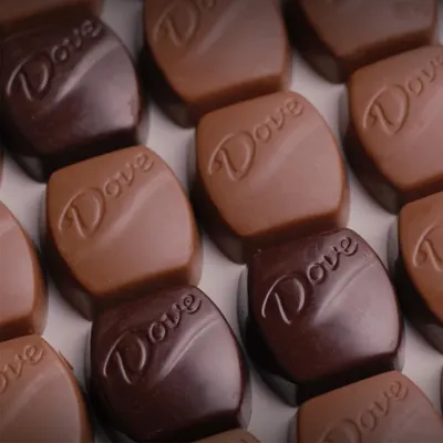 Showcases the Dove brand identity through embossed logo on chocolate pieces in multiple varieties (milk and dark chocolate), reinforcing brand recognition and product range.