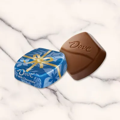 Shows the Dove chocolate product both wrapped in its decorative blue packaging with gold ribbon and unwrapped to display the chocolate piece with embossed branding, giving shoppers a clear view of…