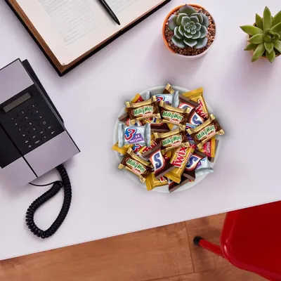 Demonstrates the product in a real-world office environment to help shoppers visualize the candy assortment as a workplace snack option or desk accessory.
