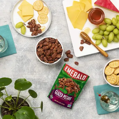 Showcases the product in a real-world entertaining context with complementary foods to help shoppers visualize how the glazed pecans fit into a charcuterie or snacking occasion.