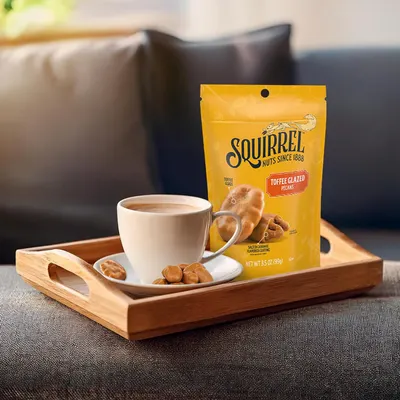 Showcases the product in a cozy, real-world home environment to help shoppers visualize enjoying the toffee glazed pecans as a snack with coffee or tea.