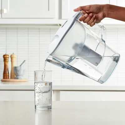 Shows the water filter pitcher being used in a real kitchen environment, demonstrating ease of use and pouring functionality to help shoppers visualize the product in their daily routine.