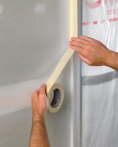 Demonstrates how to properly apply masking tape to protect surfaces during painting or renovation work, showing the ease of use and proper technique.
