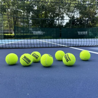 Showcases the tennis balls in their natural use environment on a tennis court, helping shoppers visualize the product in real-world play without any distracting text or feature callouts.