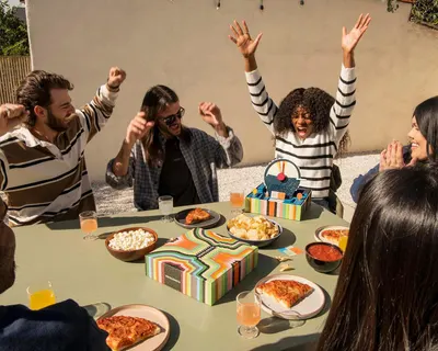 Shows the product being enjoyed in a real-world social setting with friends celebrating, helping shoppers visualize the product as part of fun gatherings and parties.