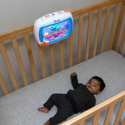 Shows the product in a real-world nursery setting with a baby in a crib, demonstrating how the product naturally fits into the bedtime routine and engages infants.