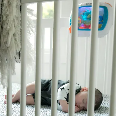 Shows the product in a real-world nursery environment with a sleeping baby, demonstrating the crib's practical use and creating an emotional connection with parents.