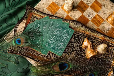 Displays the playing cards in an elegant lifestyle setting with ornate tray, peacock feathers, shells, and chess board to convey premium quality and sophisticated aesthetic appeal.