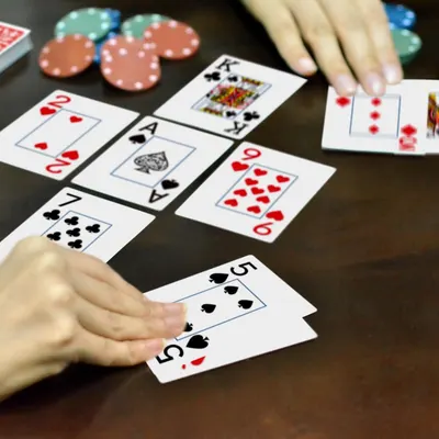 Shows the playing cards being used in an authentic poker/card game setting with hands, chips, and table to help shoppers visualize the product in real use.