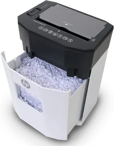 Shows the paper shredder with its pull-out waste bin filled with shredded paper, demonstrating the product's functionality and waste collection feature in a clean catalog-style presentation.