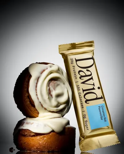 Provides a clean, catalog-style view of the protein bar product alongside cinnamon rolls to visually communicate the flavor profile and appeal to shoppers looking for a simple product presentation.