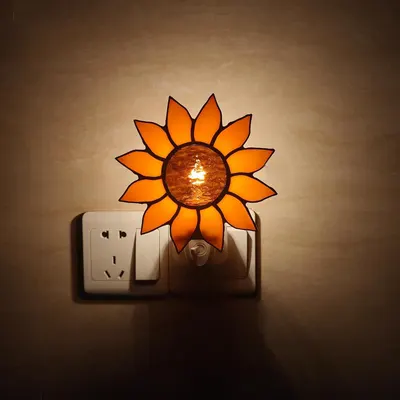 Displays the night light illuminated and plugged into a wall outlet in a real-world setting to show how it looks when in use.