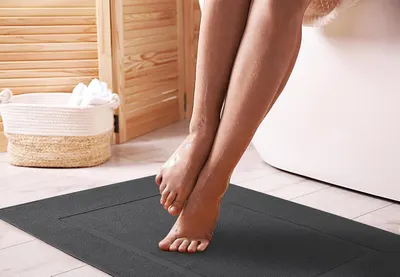 Shows the bath mat in a real-world bathroom setting with wet feet stepping on it, demonstrating its practical use after showering or bathing.