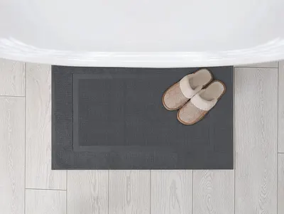 Displays the bath mat from an overhead perspective in a home setting with slippers, showing its size and how it fits in a real space.