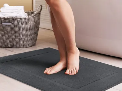 Shows the bath mat in use in a bathroom setting with feet standing on it, demonstrating its comfort and practical application.