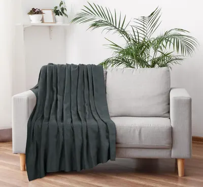 Shows the blanket draped over a sofa in a living room setting, demonstrating its versatility for use beyond the bedroom without any text overlay.