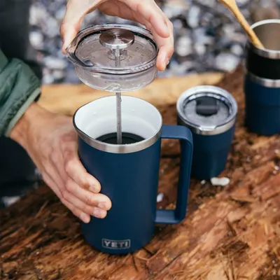Shows the coffee press being used in a real outdoor setting to help shoppers visualize the product in use during camping or outdoor activities.