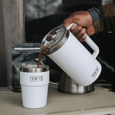 Demonstrates the product in use by showing someone pouring coffee from the press into a tumbler in a real-world setting.
