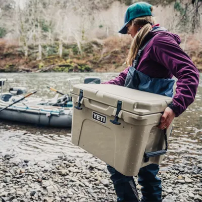 Demonstrates the cooler in a real-world outdoor setting with a person carrying it by a river, showing its portability and rugged use context without any text…