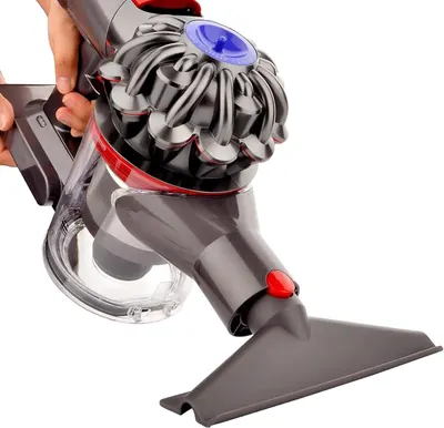 Shows the vacuum attachment in real-world use attached to a Dyson vacuum cleaner with no text overlay.