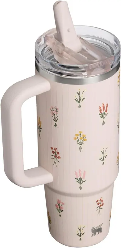 Displays the full tumbler with its decorative floral pattern and handle design in a clean lifestyle setting with no text overlay.