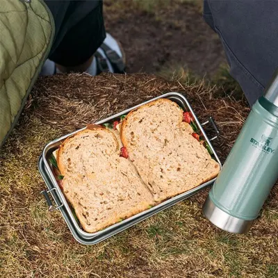 Shows the product in a real-world outdoor camping context with a sandwich inside, demonstrating practical use without any text overlay.