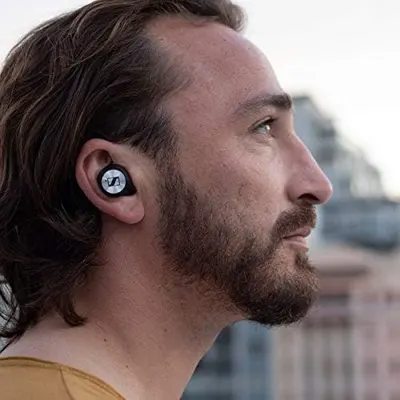 Shows the earbud worn naturally in an outdoor city setting so shoppers can picture everyday use. No text or callouts are used.