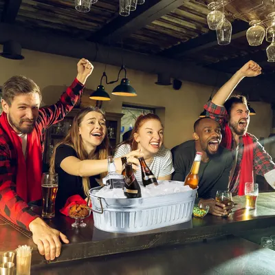 Shows the product in a real social setting with friends cheering at a bar, conveying fun and good times without any text overlay.