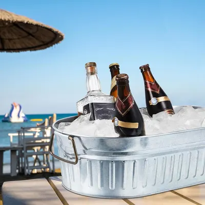 Shows the galvanized tub filled with ice and drinks in a relaxed beach setting so shoppers can picture using it for outdoor gatherings. No text overlay is present.
