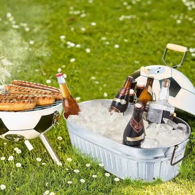 Shows the soccer ball themed grill and galvanized ice tub in a relaxed outdoor garden setting, suggesting a fun summer barbecue or football viewing party.