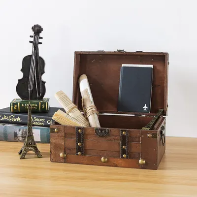 Shows the vintage wooden trunk styled on a real desk with books, a passport, and rolled papers to suggest its use as a decorative keepsake storage piece in a home setting.